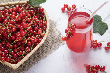 Sprigs of red currant berries are lying in a wicker plate, a Morse of berries is in a glass glass on a light background