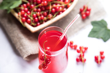 Sprigs of red currant berries are lying in a wicker plate, a Morse of berries is in a glass glass...