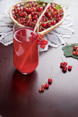 Sprigs of redcurrant berries lie on a wicker plate, and a Morse of berries stands in a glass glass and a tube on a dark table with a knitted napkin. A summer drink that quenches your thirst.
