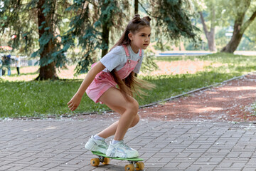 Pretty brunette girl rides a board in park. Sports lifestyle. Summer holidays.