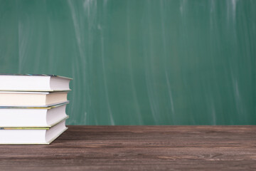 Close-up photo of stack of texbooks  isolated on green chalkboard and wooden table copyspace