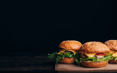 three homemade hamburgers with meat, cheese, lettuce, tomato on a wooden Board on a table on a black background