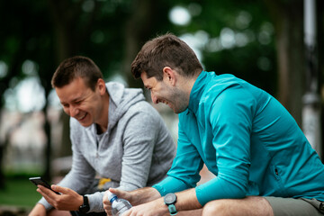 Fit young men taking rest from running. Two friends training outdoors.	