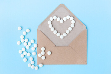 Open craft envelope on a light blue background. White pills in the form of a heart. The tablets are scattered. View from above. Letter, message, news. Medicine, protection against diseases, viruses