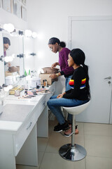 African American woman applying make-up by make-up artist at beauty saloon.