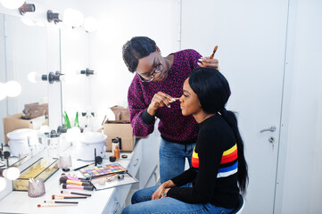African American woman applying make-up by make-up artist at beauty saloon.