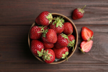Delicious ripe strawberries in bowl on wooden table, flat lay