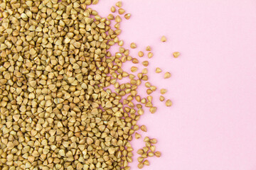 Brown raw buckwheat grains on pink paper background. Copy space for text.