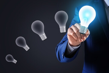 Idea concept. Businessman touching glowing light bulb on virtual screen, closeup