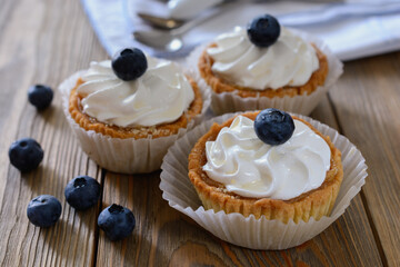 Three shortcrust tartlets with whipped egg white cream on top, garnished with blueberries on a wood table