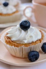 Shortcrust tartlets with whipped egg white cream on top, garnished with blueberries next to cup of tea, vertical orientation