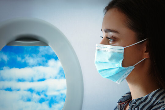 Traveling By Airplane During Coronavirus Pandemic. Woman With Face Mask Near Porthole