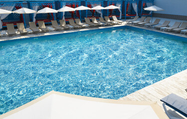 Fototapeta na wymiar Lounge chairs with umbrellas near swimming pool on sunny day
