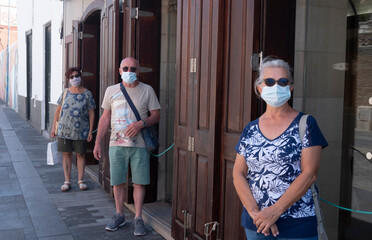 Three elderly people standing in the street at a social distance because of the coronavirus wait to...