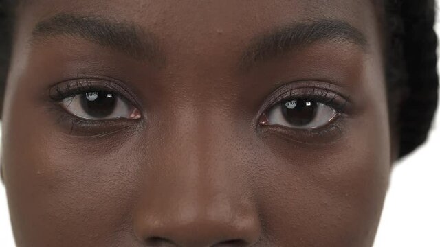 Close-up of opened brown eyes of young black woman. Moving eyes to left and right. Isolated on white background