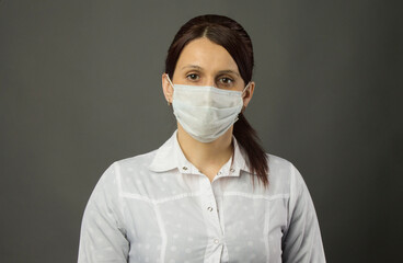 Female doctor in a mask. Young woman in medical mask and gown standing straight and looking at the camera, medium shot.