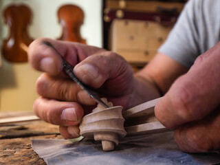 Hands of luthier violin maker carving and working on a instrument scroll  in his workshop in...