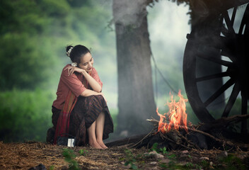 A woman sitting beside a fire and a buffalo in a rural field.