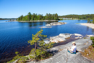 A woman on the rocky shore of Koyonsaari Island (southern part) overlooking Erosaari Island. Ladoga lake. Karelia. Russia