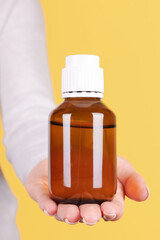Hand with medicine bottle, chemistry container. Isolated on yellow background.