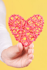 Hand with red wooden heart decoration. Isolated on yellow background.