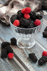 blackberries and raspberries in a glass container on a wooden background. Textile. Wild flowers,...