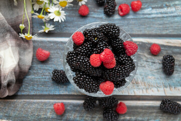 blackberries and raspberries in a glass container on a wooden background. Textile. Wild flowers,...