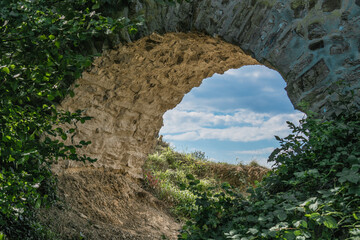 View through the half-buried passage through a castle wall against the slightly cloudy sky.