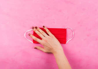 Red face mask in female hand on pink. Covid-19