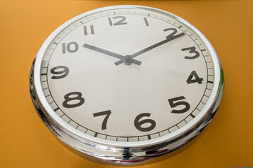 A simple mirrored round watch is taken at a bottom angle against a light brown background.