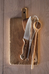 Kneif, whisk and kitchen utensils on a wooden cutting board on a table
