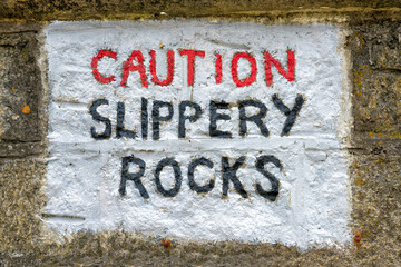 Caution Slippery Rocks sign painted on rocks, United Kingdom