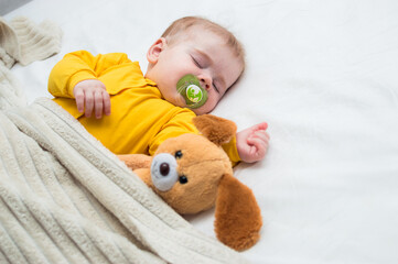 Close-up portrait of a sleeping kid in an embrace with a toy and a pacifier in his mouth.