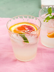 Fresh summer iced citrus drink with lime, mint and blood oranges on pastel pink napkin