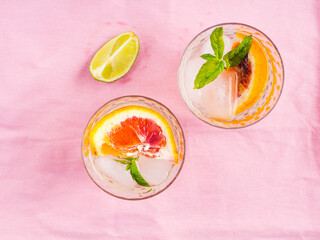 Fresh summer iced citrus drink with lime, mint and blood oranges on pastel pink napkin