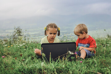 Pupil sitting on green grass outdoor and using laptop for distant studying