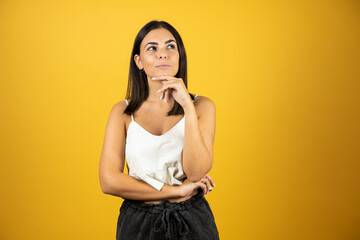 Young beautiful woman thinking about something. Looking to the right, standing over yellow background