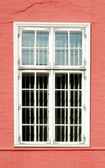 altes, verziertes weisses Fenster an einer roten Hauswand
