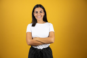 Young beautiful woman standing over yellow isolated background smiling with her arms crossed