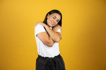 Obraz premium Beautiful young woman on an isolated background hugging herself happy and positive, smiling confident. Self-love and self-care