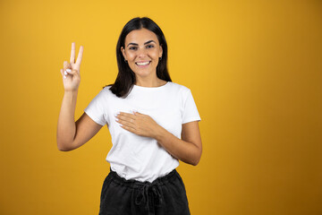 Young woman wearing over isolated yellow background Swearing with hand on chest and fingers, making a loyalty promise oath - obrazy, fototapety, plakaty