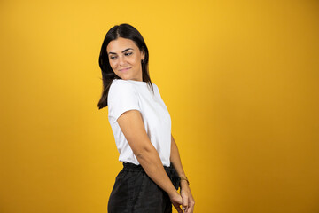 Young beautiful woman in profile over isolated yellow background smiling and looking back