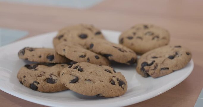 Extreme close-up of plate with biscuits standing on the table as little Caucasian child's hand taking one cookie. Unrecognizable kid having lunch with sweet tasty bakery at home.