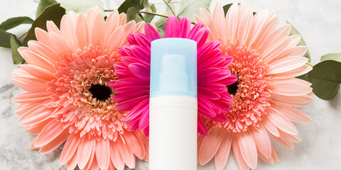 Face moisturizer over pink flowers. Beauty skin care products concept banner - 367101551