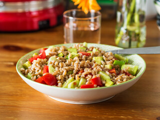 Fresh Italian farro spelt salad with tomatoes, avocado and cucumbers on wooden kitchen table. Easy recipe whole food meal