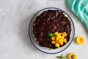 Delicious no baked cheesecake with fresh apricots, chocolate glaze and mint. Light grey stone background. Top view.