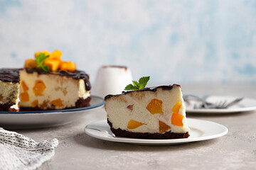 Sliced no bake apricot cheesecake garnish with chocolate glaze, fresh apricots and mint, light stone background. Delicious summer dessert.