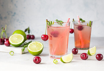Cocktail or lemonade with cherries, lime and rosemary on a grey concrete table. Summer refreshment...