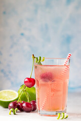 Lemonade or non-alcohol cocktail with cherry and lime in glass on grey stone background. Summer berry drink.