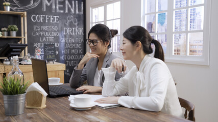 Two young businesswomen having successful meeting at cafe restaurant. beautiful office ladies coworkers sitting in modern cafeteria. female colleagues smiling looking laptop computer in coffeehouse